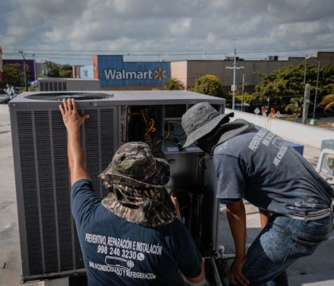 Two HVAC technicians installing a rooftop air conditioning condenser unit