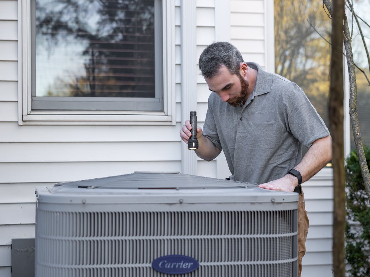 HVAC technician inspecting a residential Carrier air conditioner condenser unit