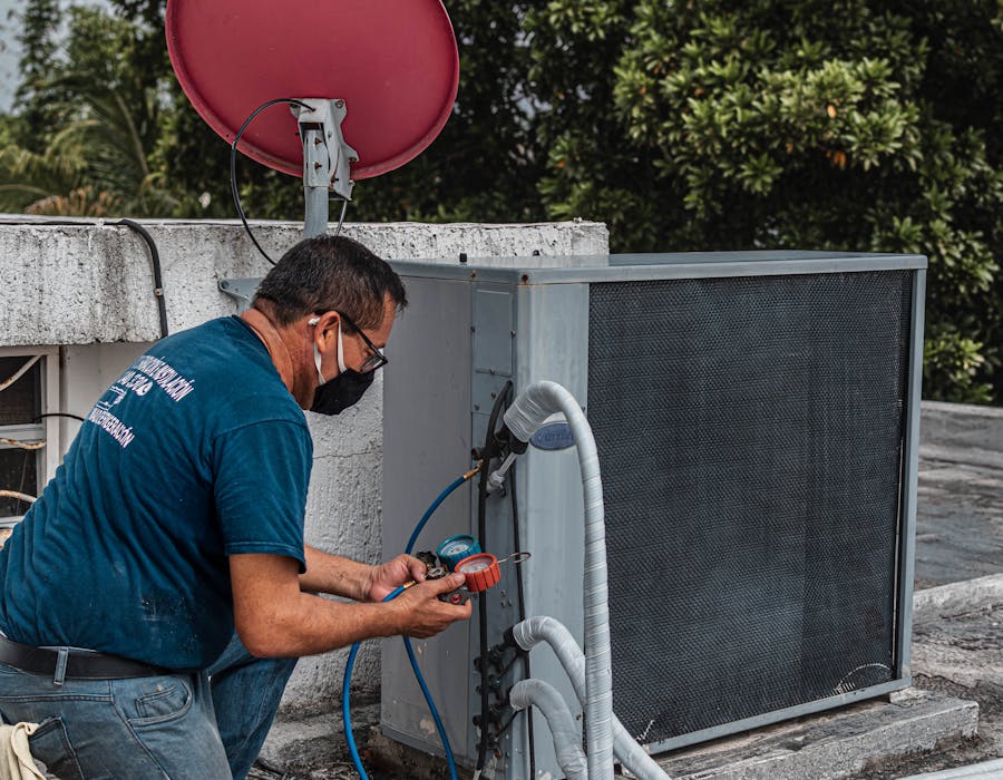 HVAC technician using a manifold gauge to service a rooftop air conditioning unit