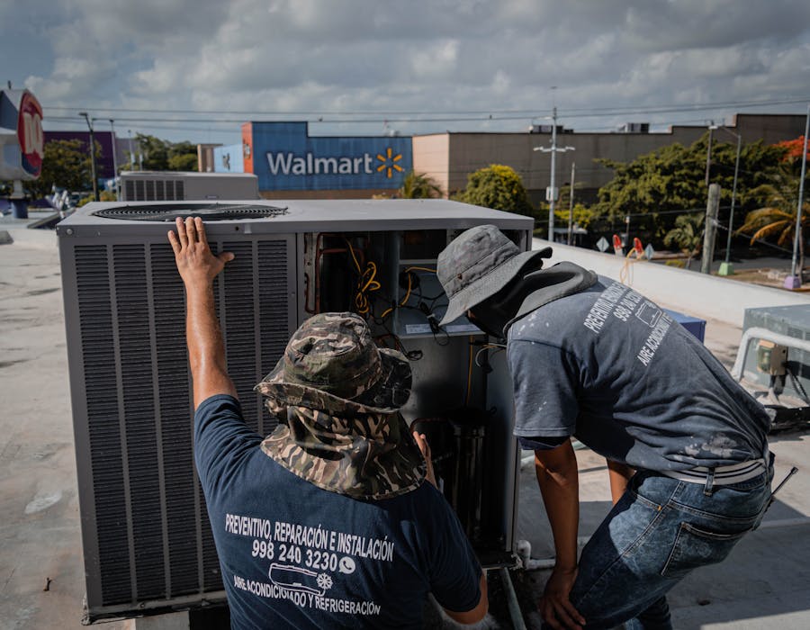Two HVAC technicians installing a large commercial rooftop air conditioning condenser unit