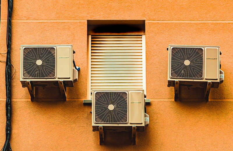 Three air conditioning condenser units mounted on an exterior building wall
